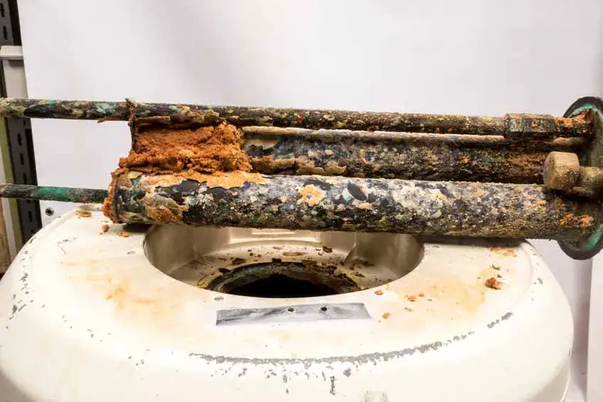 Two corroded metal rods covered in brown, crusty buildup rest on top of a circular opening in a white tank, possibly part of a water softener or filtration system.